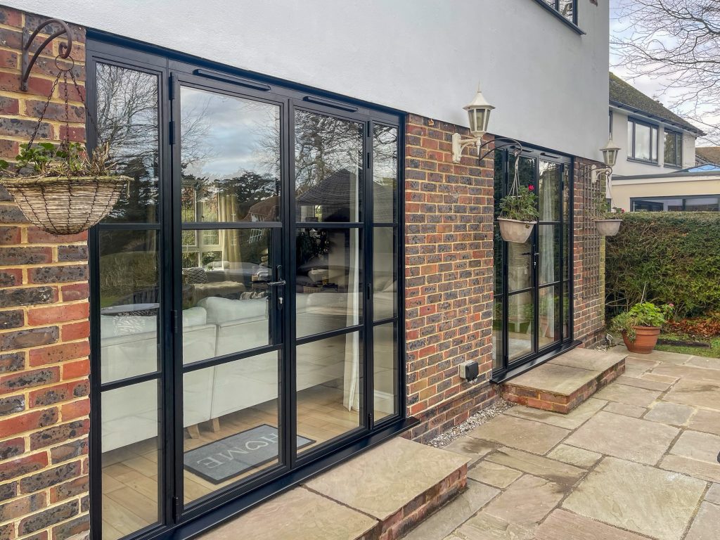 Steel look French doors with side panels in black aluminium opening onto a patio in Eastbourne